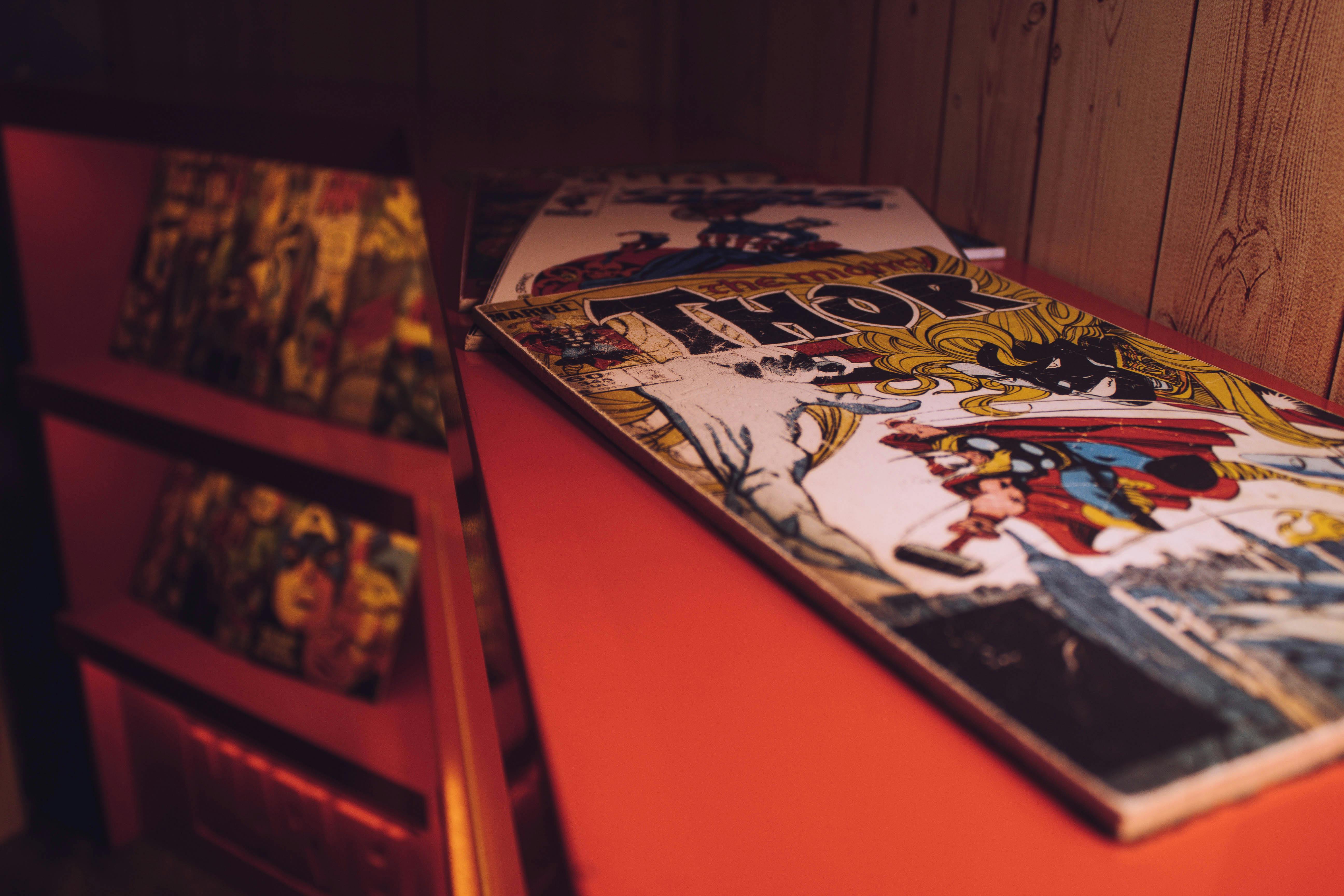 Comic books displayed on red retail shelf with wooden backdrop, representing small business merchandise presentation in specialty leasing spaces like mall kiosks or pop-up shops